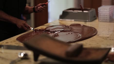 chef tempering chocolate making process with spatula on granite counter