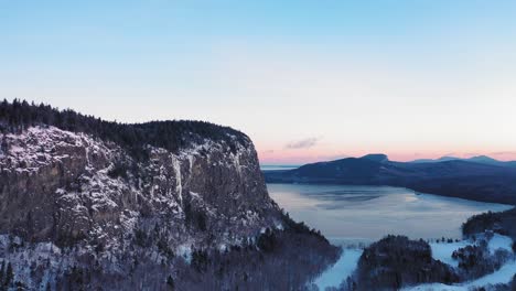 aerial view looking along the edge of a cliff during a winter sunrise while flying up and to the left