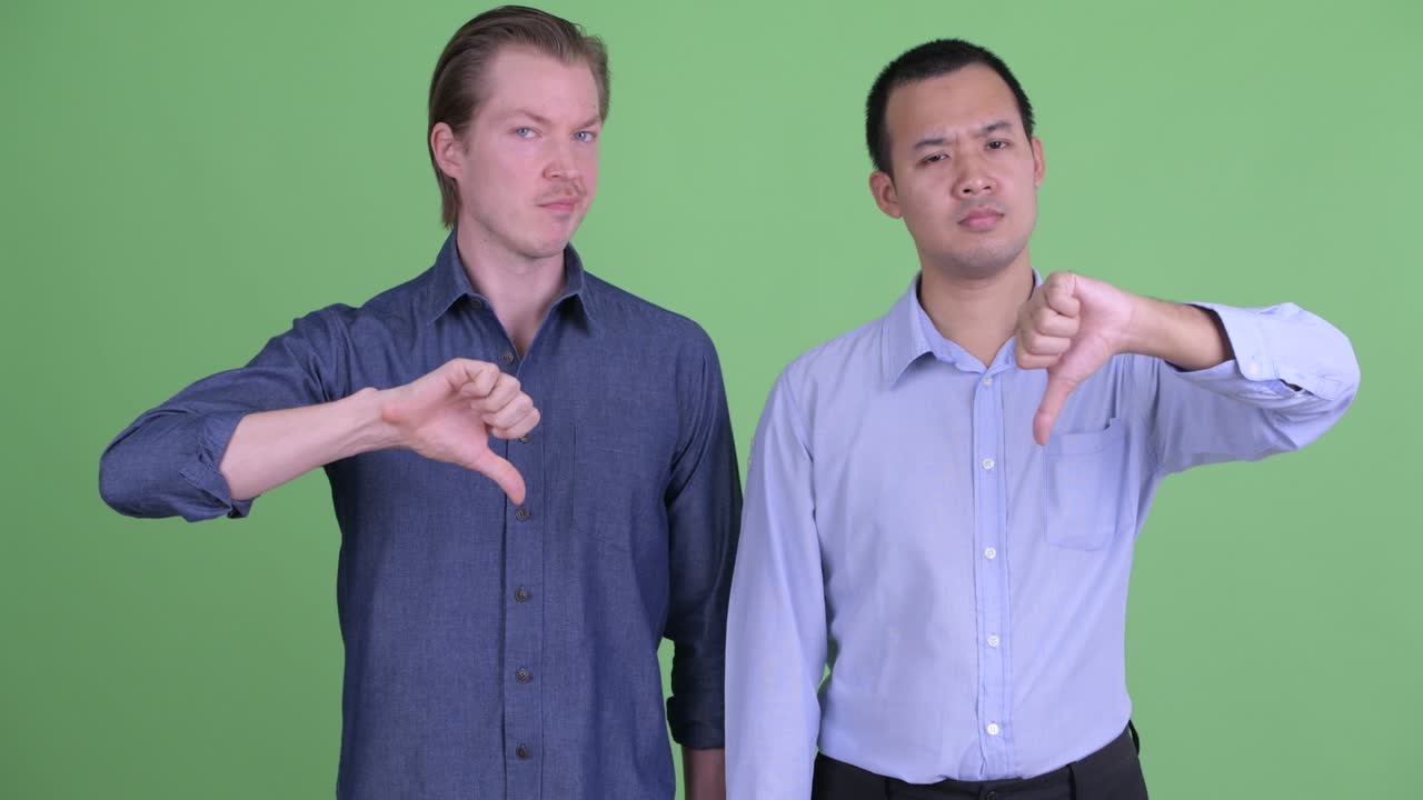 두 명의 사업가가 녹색 스튜디오 배경에 엄지손가락을 내려주고 있습니다.