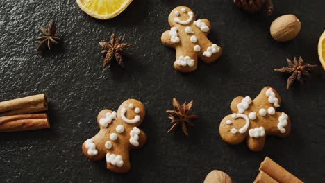 video of smiling gingerbread men and spices, slices of orange and nuts over black background