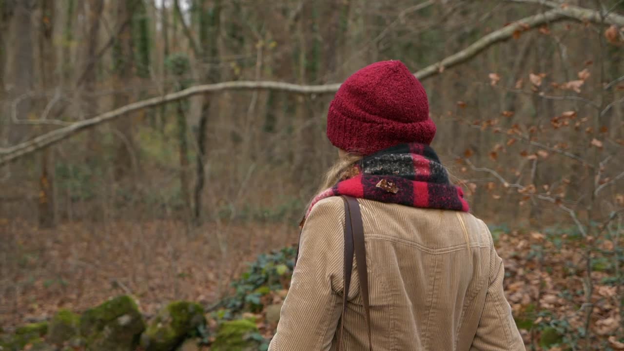 Riprese circolari dietro una donna con cappello rosso che cammina in una foresta autunnale, Slow Motion
