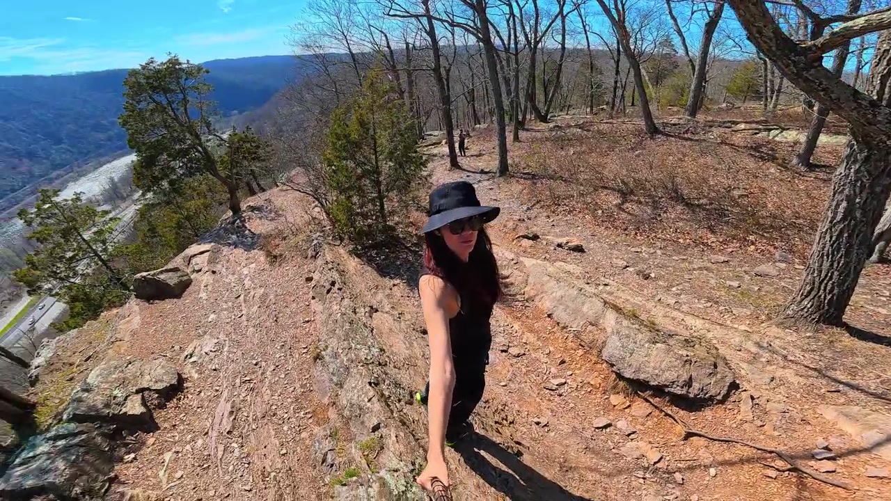 Nova Jersey, EUA, 1º de maio de 2026: Mulher caminhando em trilha rochosa de cume acima do vale do Rio Delaware. Perspectiva de grande angular de uma caminhante em um caminho pedregoso com um rio e uma rodovia visíveis abaixo