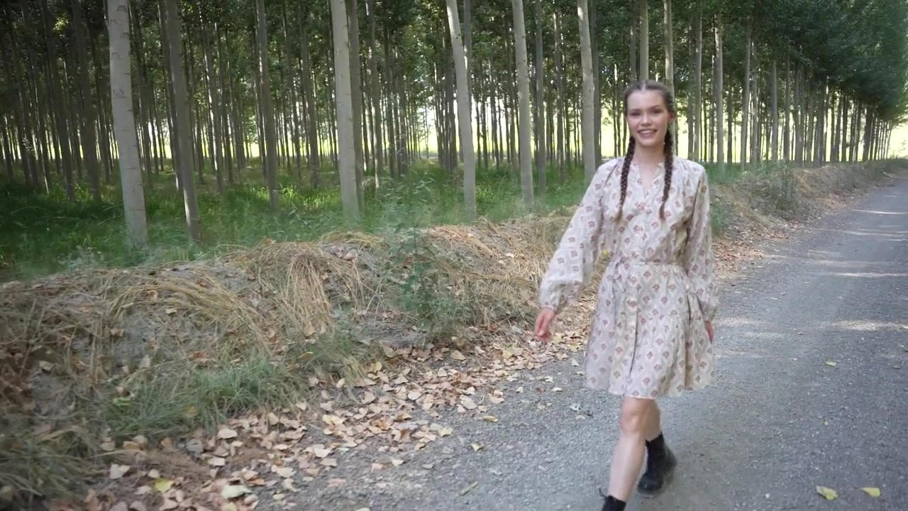 Una giovane donna con un bellissimo vestito sta camminando lungo un sentiero panoramico nel bosco, circondata dalla natura.