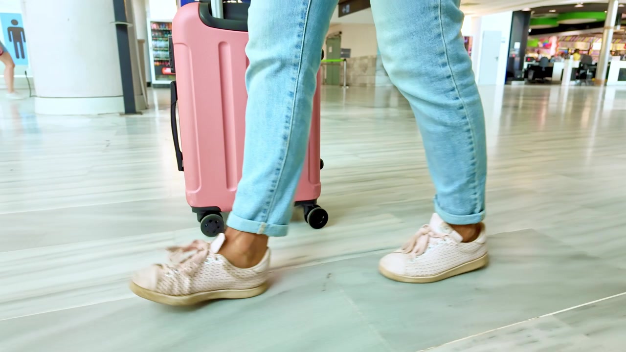 Donna che cammina con una valigia rosa in un terminal aeroportuale