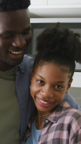 video of happy african american couple embracing in kitchen and looking at camera