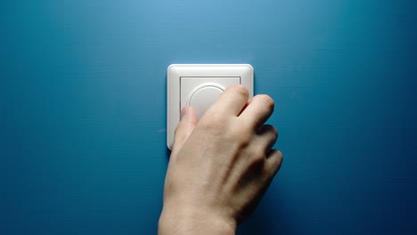 la mano humana gira el botón de atenuante en una pared azul lentamente