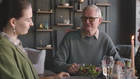 Senior-Man-Talking-With-His-Two-Adult-Daughters-While-Sitting-At-Table-And-Having-Meal-Together-At-Home