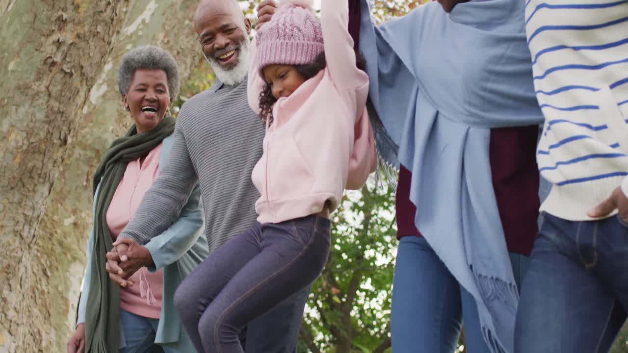 Video of happy african american parents and grandparents walking with granddaughter in garden