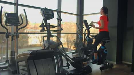 young active woman spinning a air bike in gym with trainers. female training on air bike