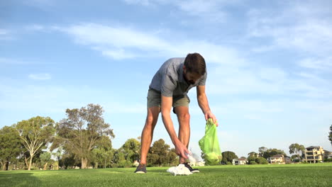 caucasian man picks up several items of trash in green park, low angle