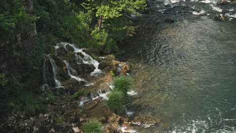 Small-waterfalls-flowing-into-a-clear-river-surrounded-by-lush-greenery-and-rocks-in-Rastoke,-Croatia