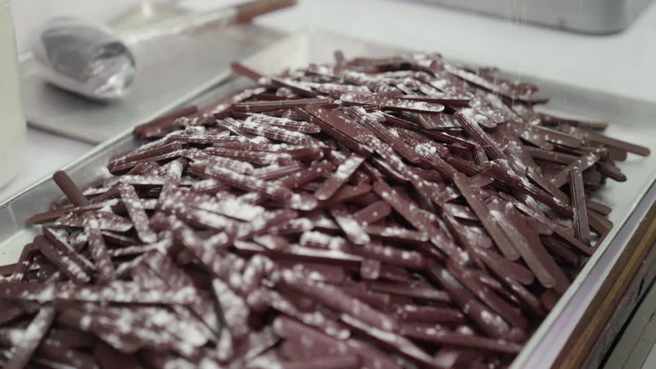 Spolverare con zucchero a velo una griglia piena di bastoncini di cioccolato fondente in pasticceria, al rallentatore