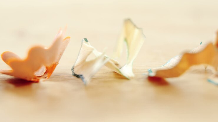 Various colored pencil shavings arranged on wooden background