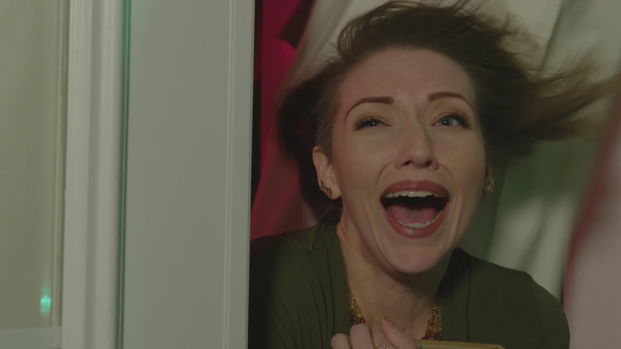 A woman opens a door and is seen screaming. The background is glowing along with wind blowing in the woman's face