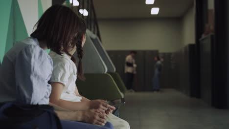 two schoolgirls smile holding smart pad in school hallway. kids enjoying break.