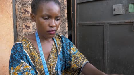 close up shot of an african womans face as she sews clothing outside her home