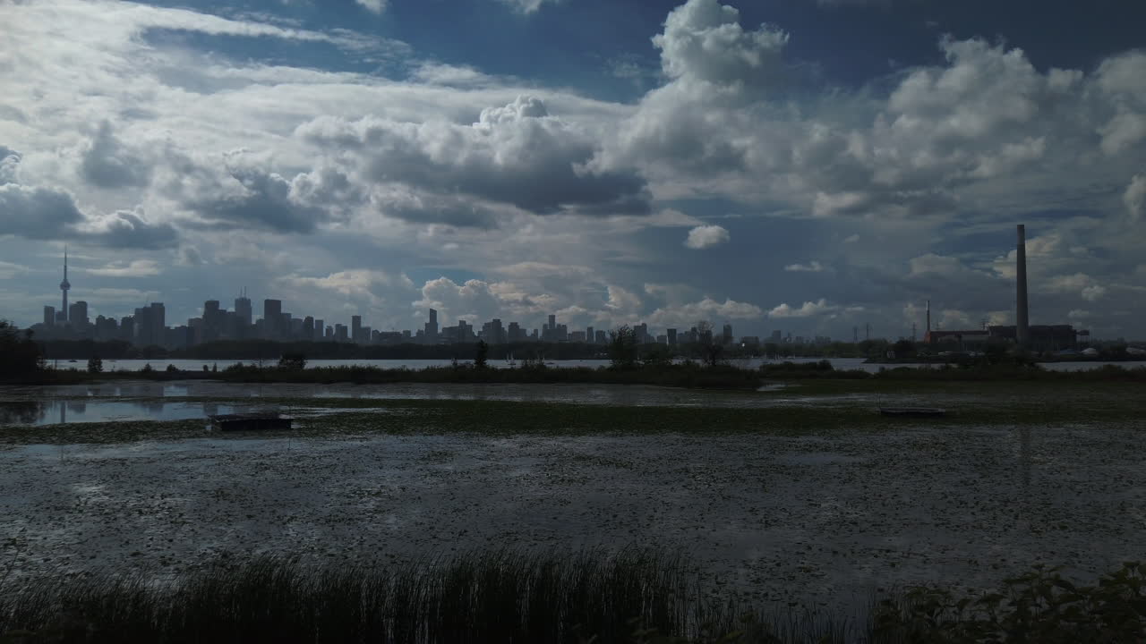 Peaceful summer view with wetlands and large pond in foreground, Toronto cityscape in the distance, and big summer sky with puffy cumulous clouds, wide exterior panning shot