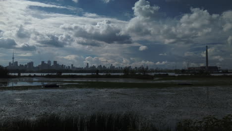 peaceful summer view with wetlands and large pond in foreground, toronto cityscape in the distance, and big summer sky with puffy cumulous clouds, wide exterior panning shot