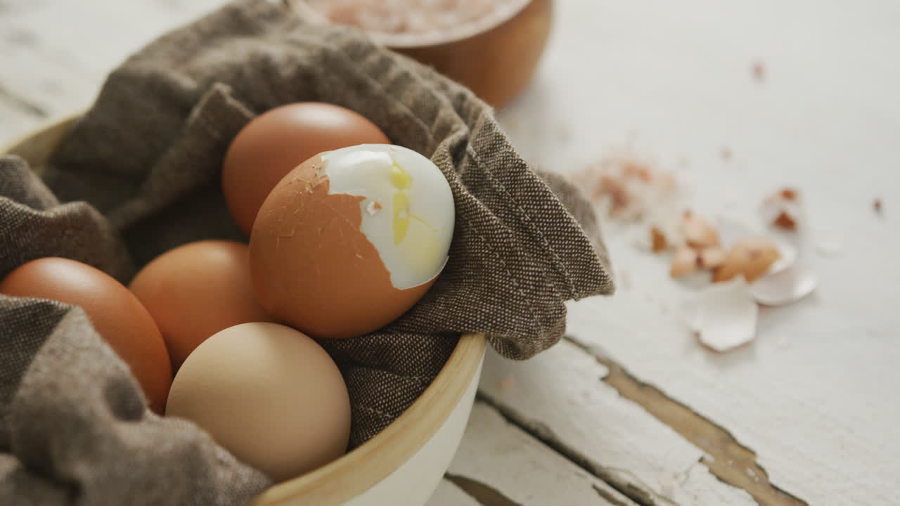 Video of close up of hard boiled brown eggs with cloth in bowl on rustic background