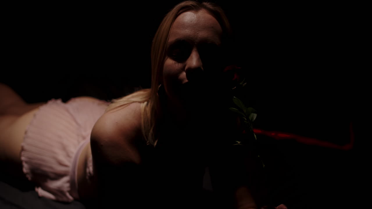 Portrait of a beautiful woman in a dark room sensually playing with a red rose