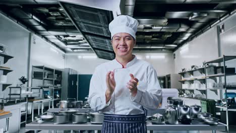 chef asiático sonriendo y aplaudiendo sus manos mientras está de pie en la cocina