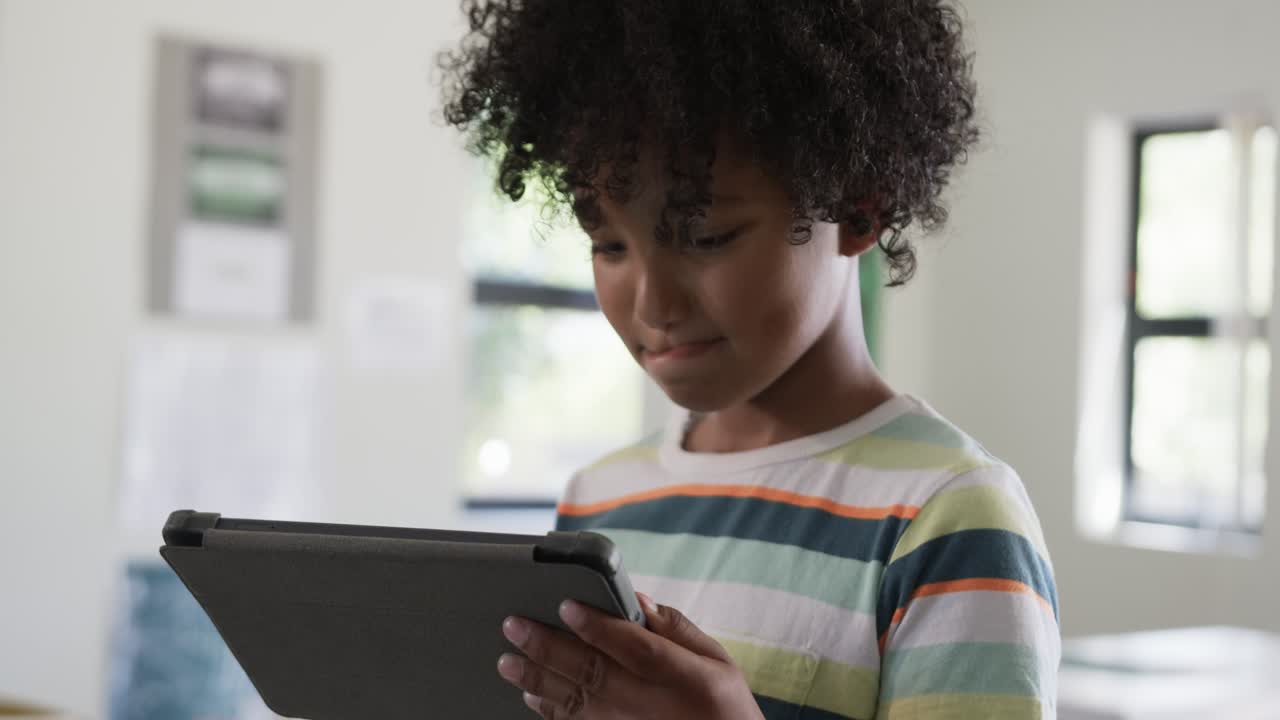 African American child reacting to tablet prompt, holding, tapping tablet in class in striped tee