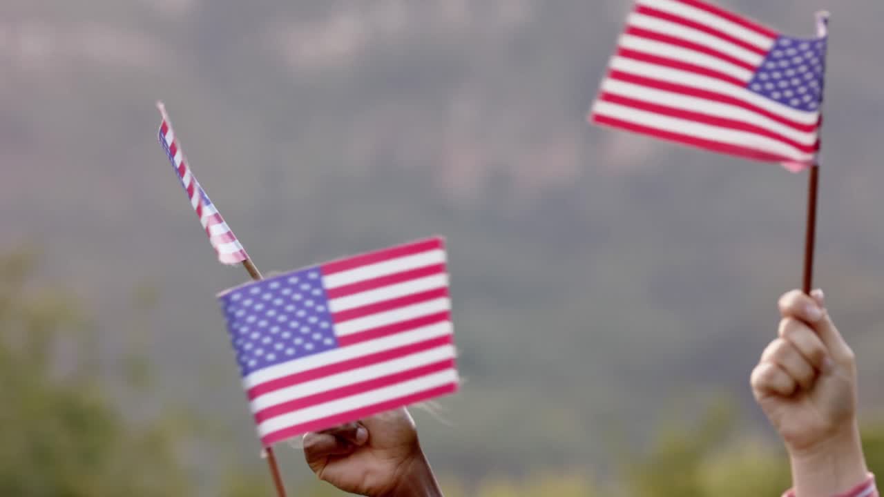Close up of hands of diverse group of friends holding flags of usa in garden, slow motion