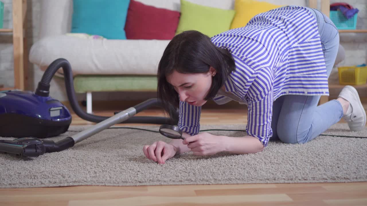 una mujer joven en la sala de estar a través de una lupa examina la alfombra en la sala