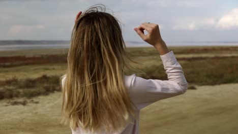 mujer relajada está bailando sola de pie en la playa de arena con los ojos cerrados, frente al agua en el fondo