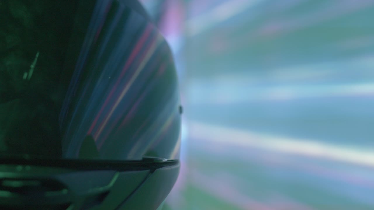 Extreme close-up of a motorcycle helmet reflecting vibrant streaks of purple and blue light. This shot creates a sense of high-speed travel through a futuristic, neon-lit city or tunnel at night.