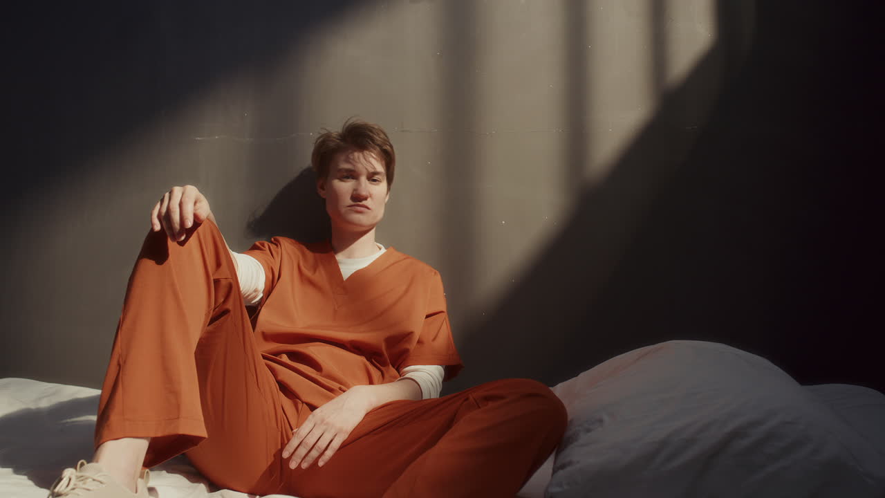 Portrait of Female Inmate Sitting on Bed in Prison Cell