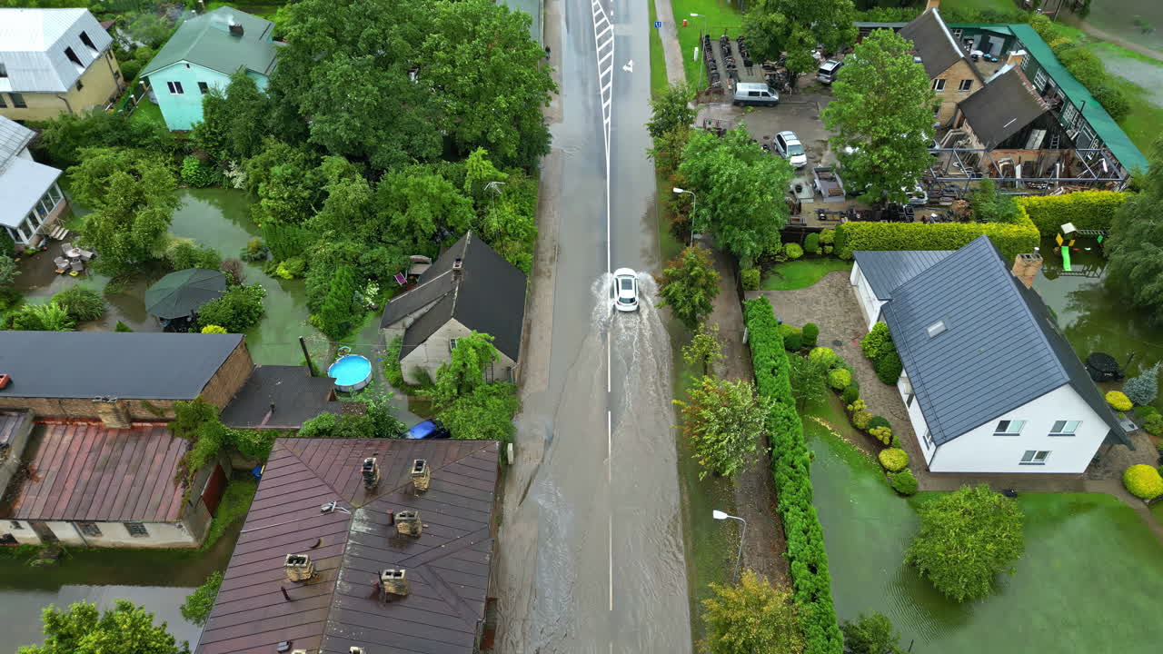 Flooded street in a village after storm and heavy rain, car drives on water street, damaged area, dolly shot in slow motion