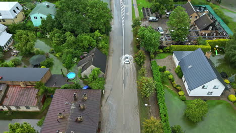 flooded street in a village after storm and heavy rain, car drives on water street, damaged area, dolly shot in slow motion