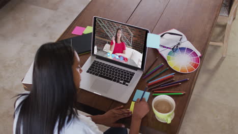 mujer caucásica usando una computadora portátil en una videollamada con una colega, tomando notas