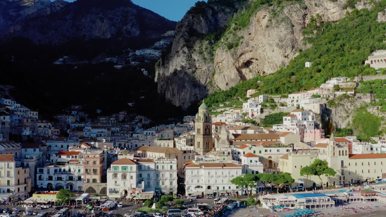 Vista aerea con drone della città di Amalfi con la Cattedrale storica, la passeggiata sul lungomare del Mar Mediterraneo e edifici dai toni bianchi sotto drammatiche scogliere montuose. Destinazione di viaggio più popolare in Italia