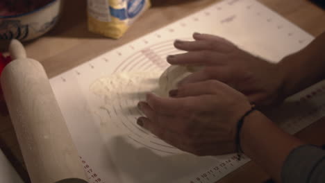 hands knead and roll dough in flour on butcher block counter with rolling pin, high angle