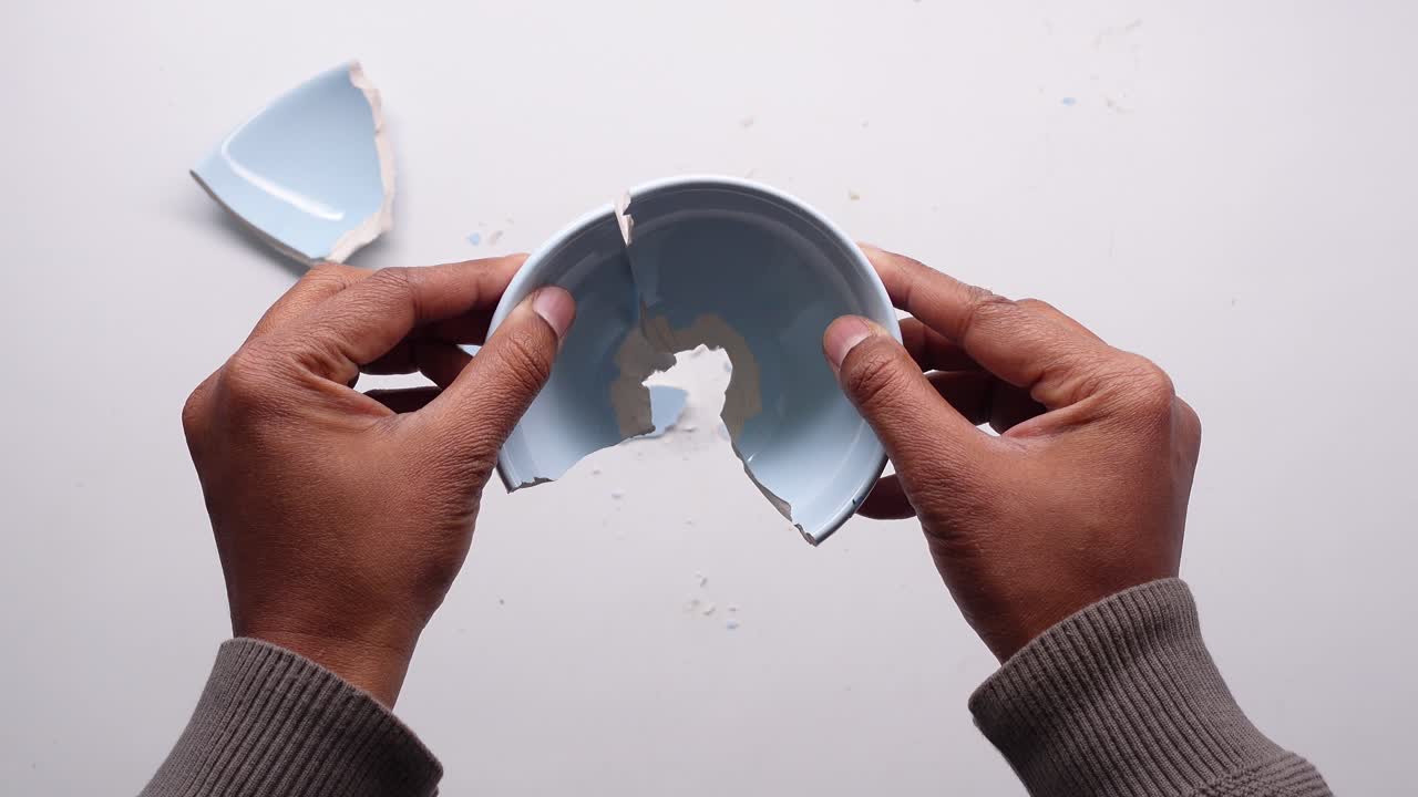 Hands Trying to Mend Broken Pieces of a Ceramic Bowl
