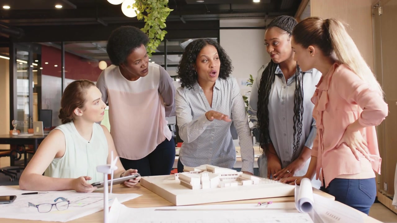 Presenter pointing at model, pink labels appearing and drifting over table as team reviewing design