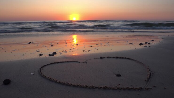 Hart symbool getekend in het zand tegen een achtergrond van zonsondergang boven de zee