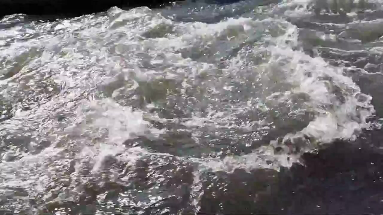Vista ravvicinata dell'acqua di fiume che scorre vigorosamente con forti correnti e riflessi scintillanti illuminati dal sole. Sfondo dinamico di movimento naturale dell'acqua
