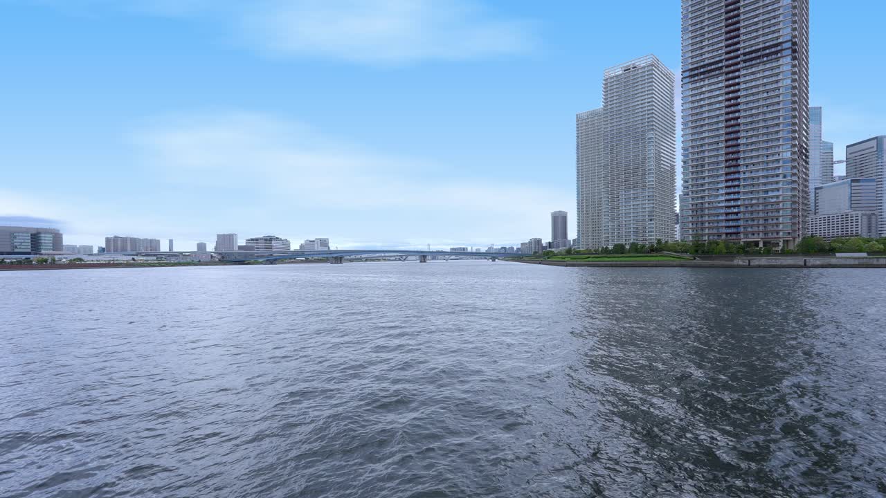 A peaceful wide shot of the Tokyo skyline from a waterfront promenade with modern high-rise buildings and a clear sky
