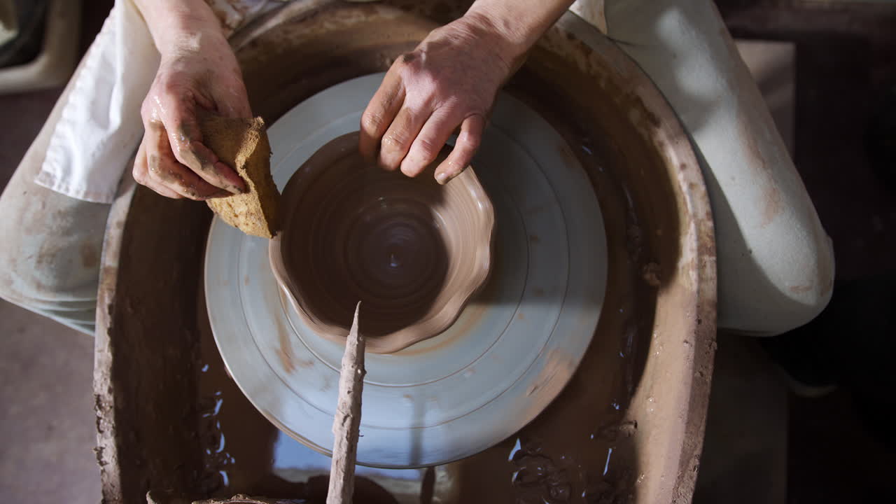 Primo piano dall'alto di un vasaio che modella l'argilla per una ciotola al tornio in un laboratorio di ceramica