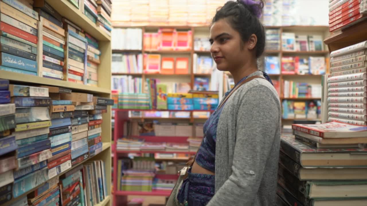 Bella ragazza asiatica in piedi che sfoglia libri tra gli scaffali, ripresa in movimento ad angolo laterale.