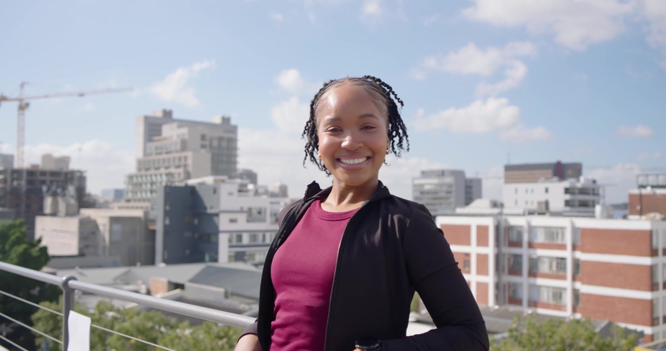 Câmera se aproximando de mulher se endireitando, virando-se, sorrindo, tocando o corrimão do terraço com roupa esportiva