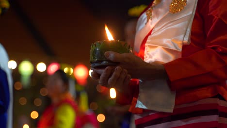 close up of female hands holding traditional yi peng festival candle at night