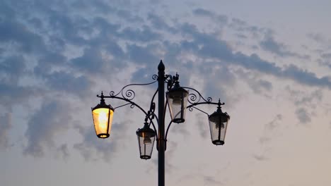 Smooth-shooting-of-a-beautiful-street-lamp-with-patterns-on-the-background-of-the-sunset-sky,-light-twilight,-fluffy-clouds