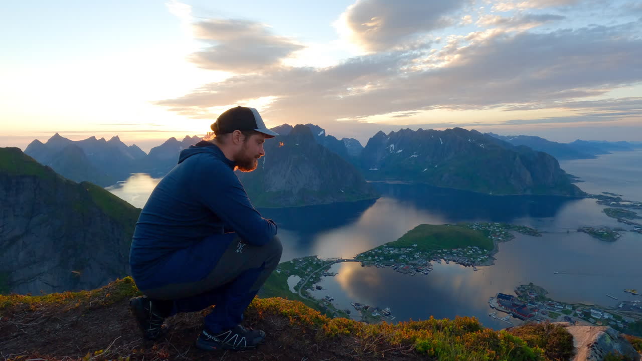 turista sentado en la cima de reinbringen en lofoten y disfrutando de la vista panorámica desde arriba