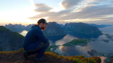 tourist sitting on the top of reinbringen in lofoten and enjoying the scenic view from above