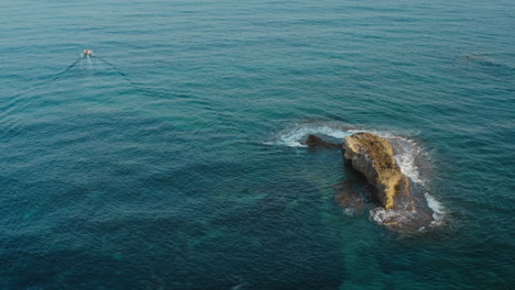 Boat-passing-a-stone-ridge-in-a-bright-blue-sea