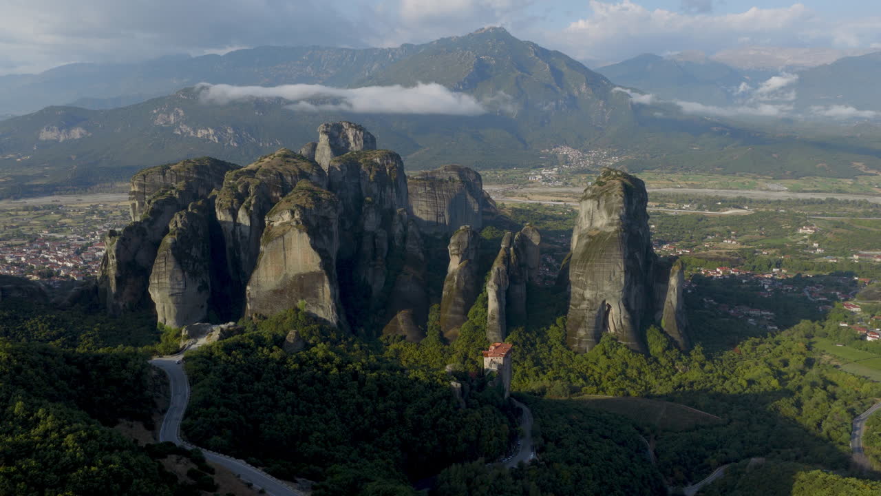 Cinematic aerial view of Meteora monastery in Greece perched on towering cliffs, dramatic rock formations and lush green valley create a breathtaking historic scene